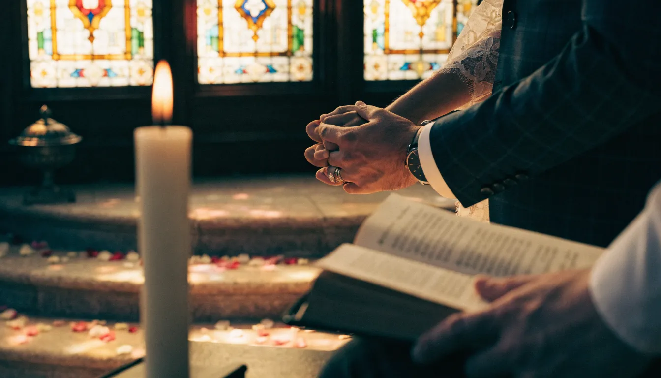 A couple's joined hands at a wedding ceremony beside a lit candle and an officiant's open book
