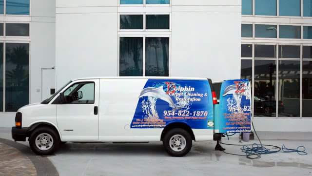 Dolphin Carpet Cleaning & Restoration branded white van with truck-mounted hoses parked outside a glass office building