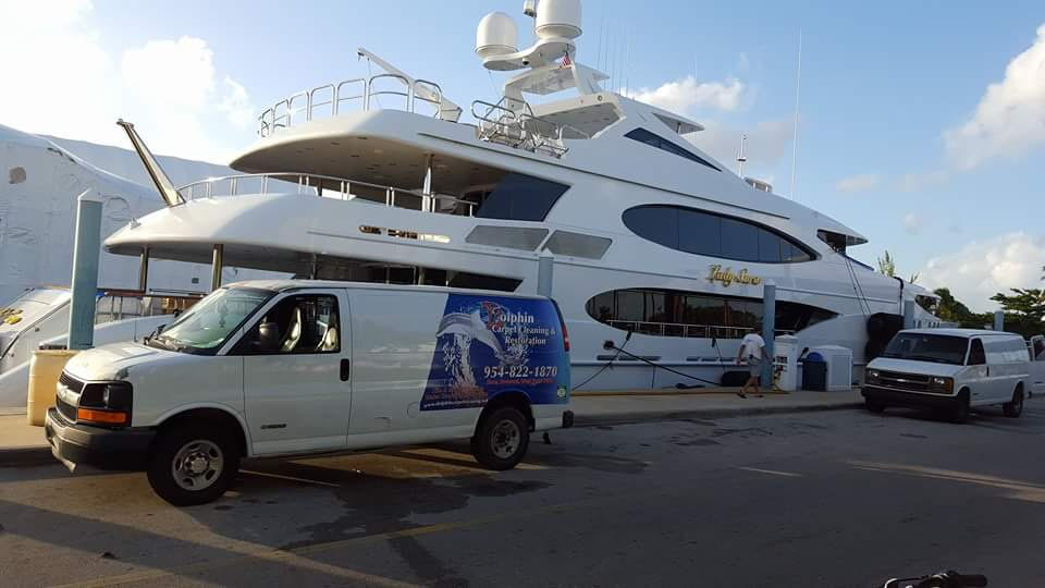 Dolphin Carpet Cleaning branded white van parked beside a large luxury yacht at a South Florida marina