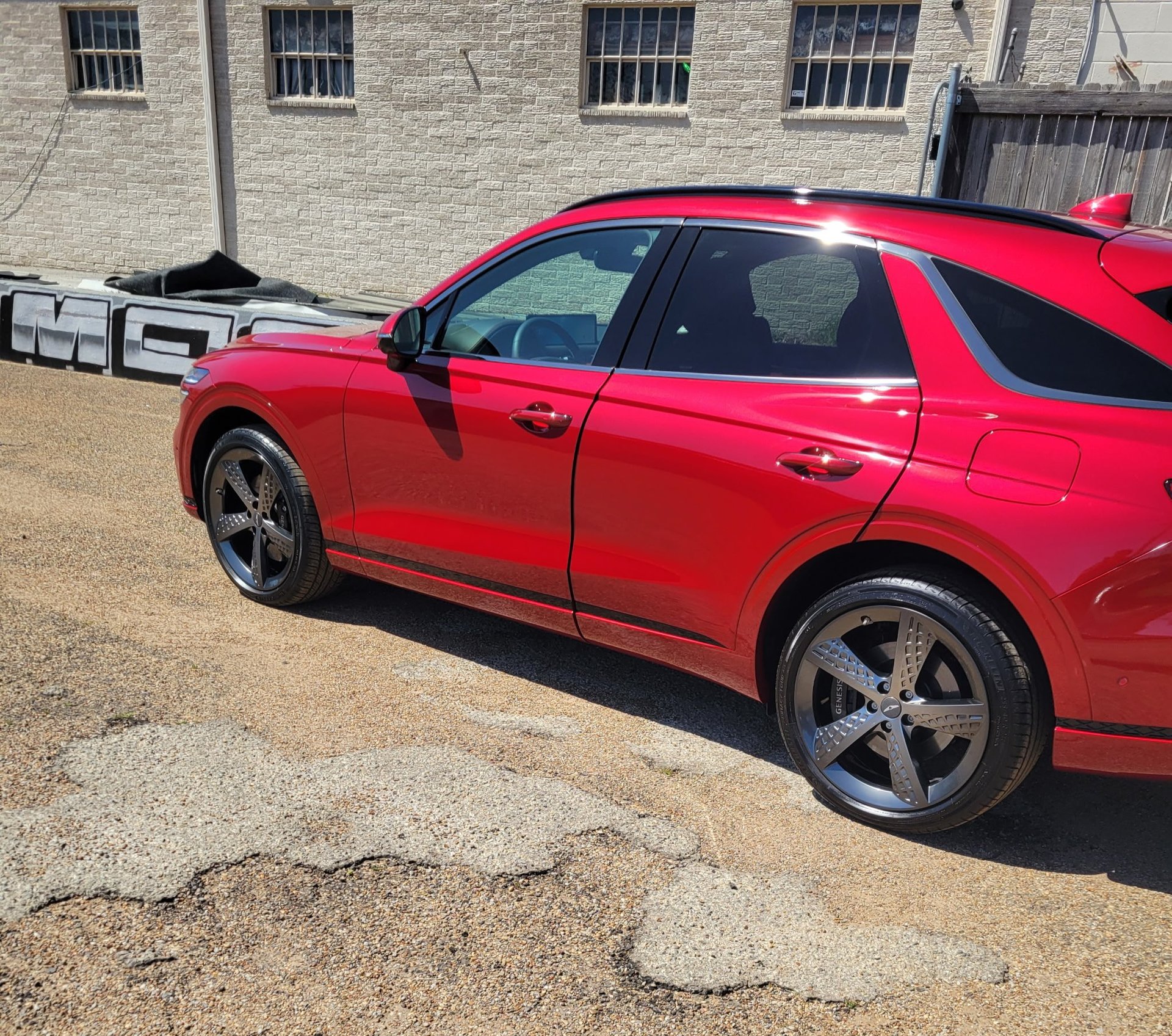 Freshly washed red Genesis SUV gleaming on the gravel lot beside the brick shop building