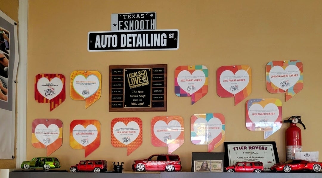Shop wall with the E Smooth Auto Detailing sign, Locals Love Us awards, a plaque and toy cars