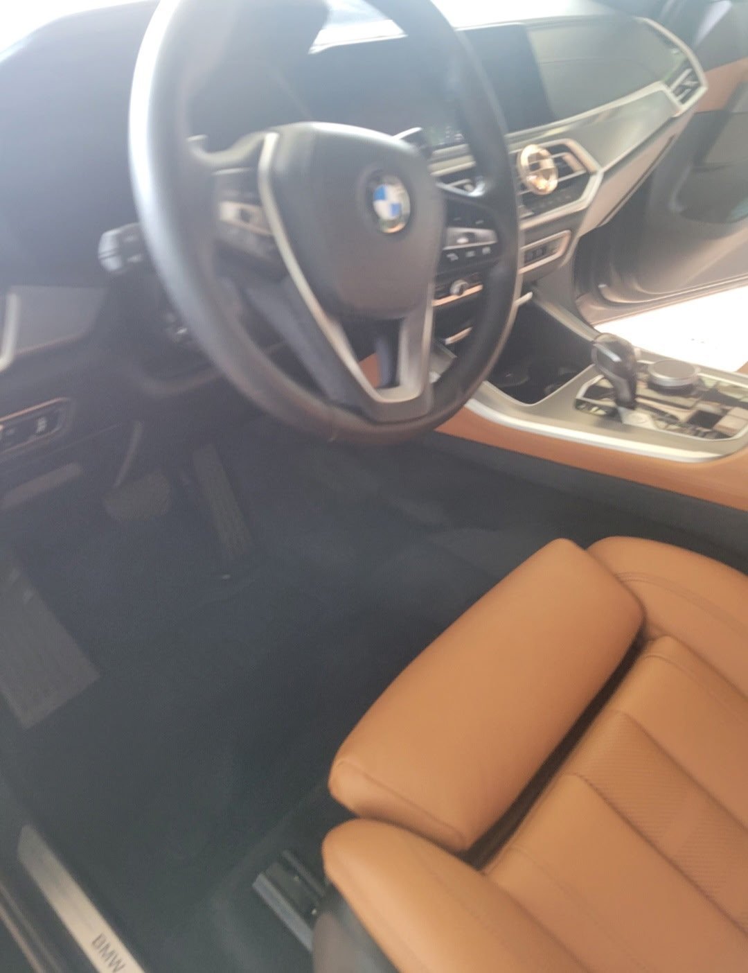 Detailed BMW interior with steering wheel, dashboard, clean floor mats and tan leather seat