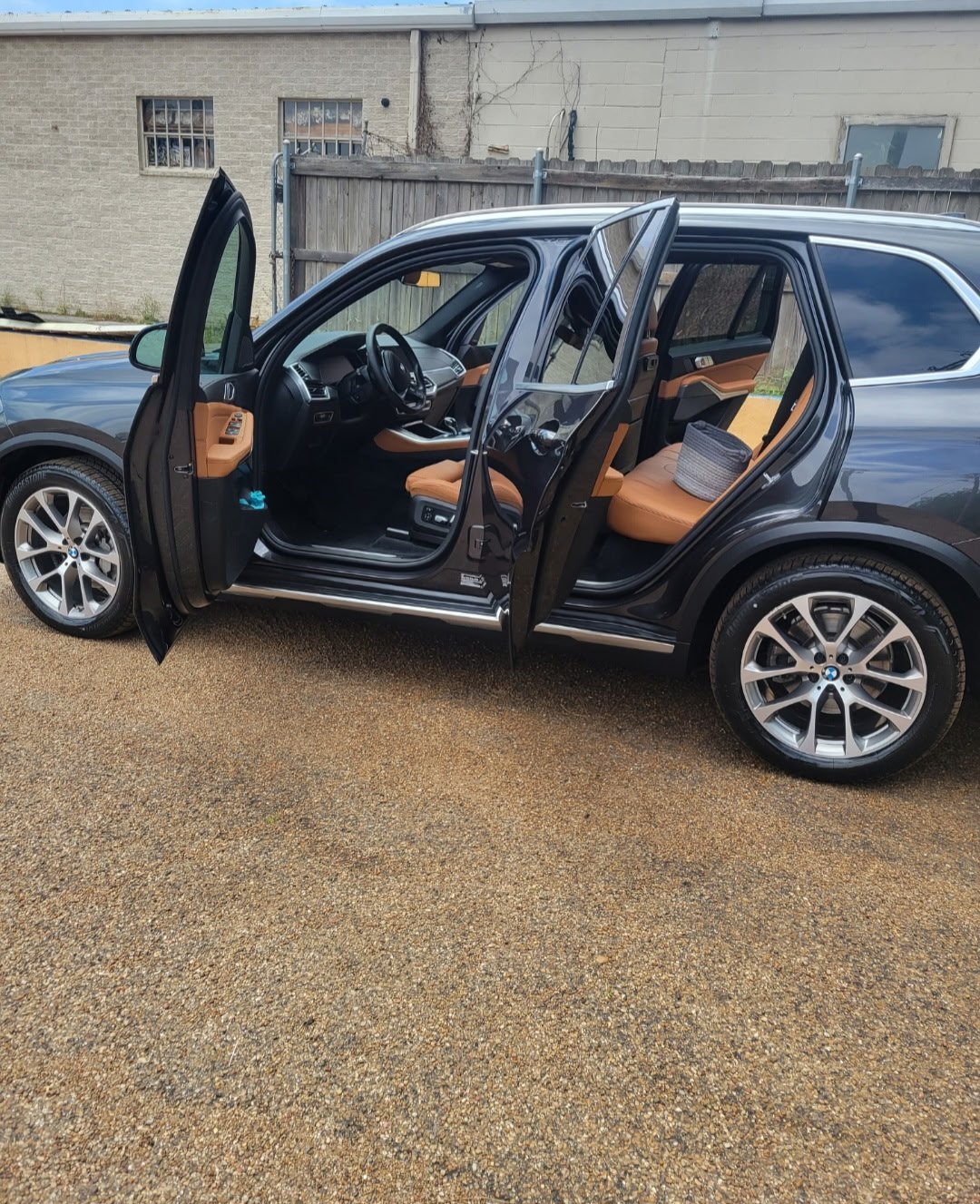 Dark BMW X5 with doors open showing a cleaned tan leather interior on the gravel lot