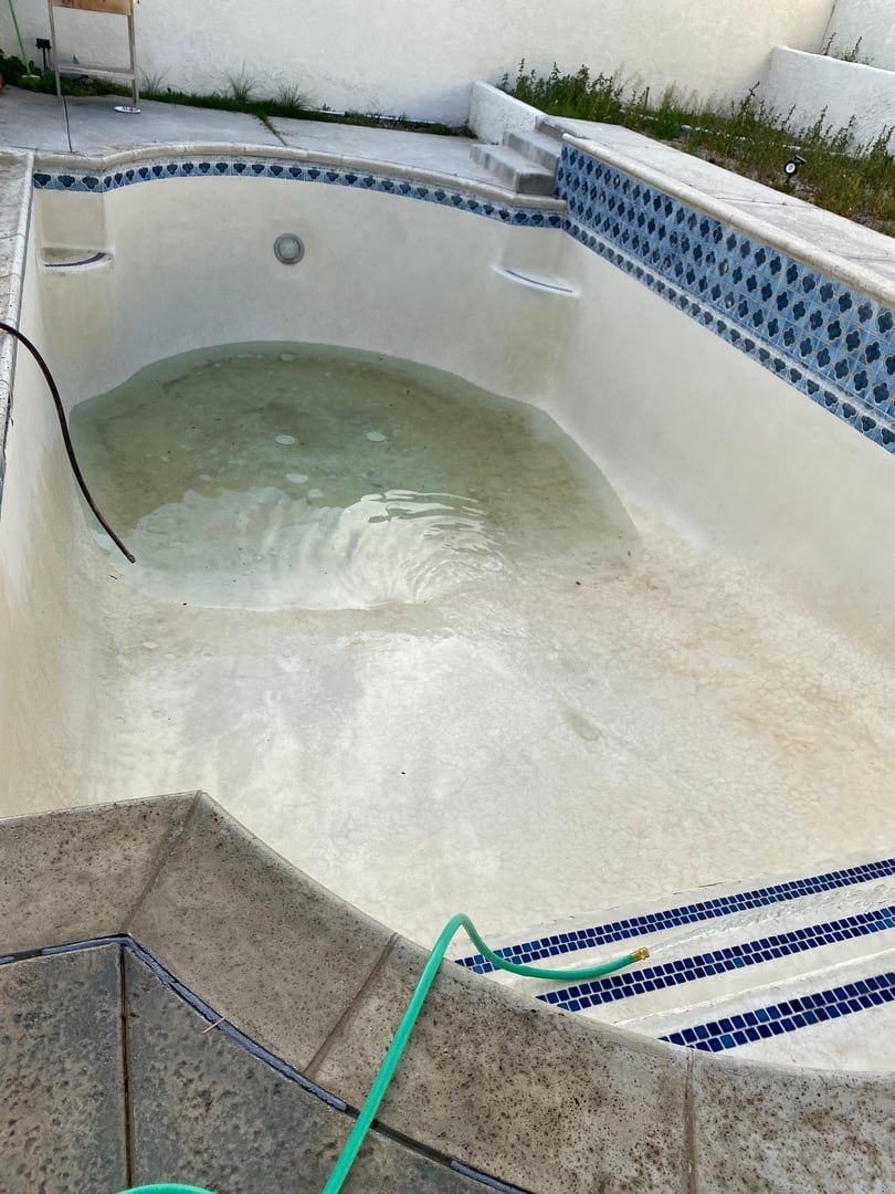 The same pool drained with cleaned white plaster and blue tile, shallow water pooling