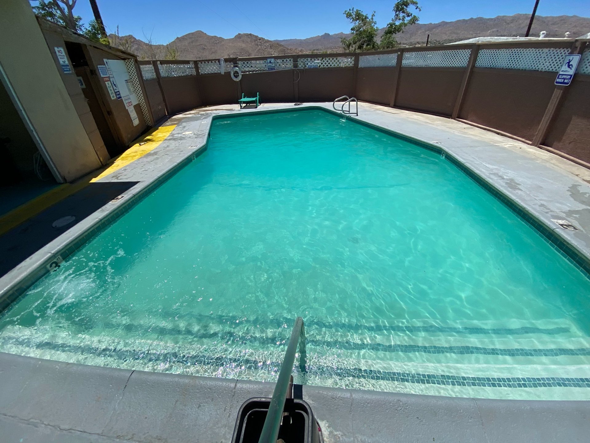 After: the same fenced pool with clear turquoise water, desert hills under a blue sky