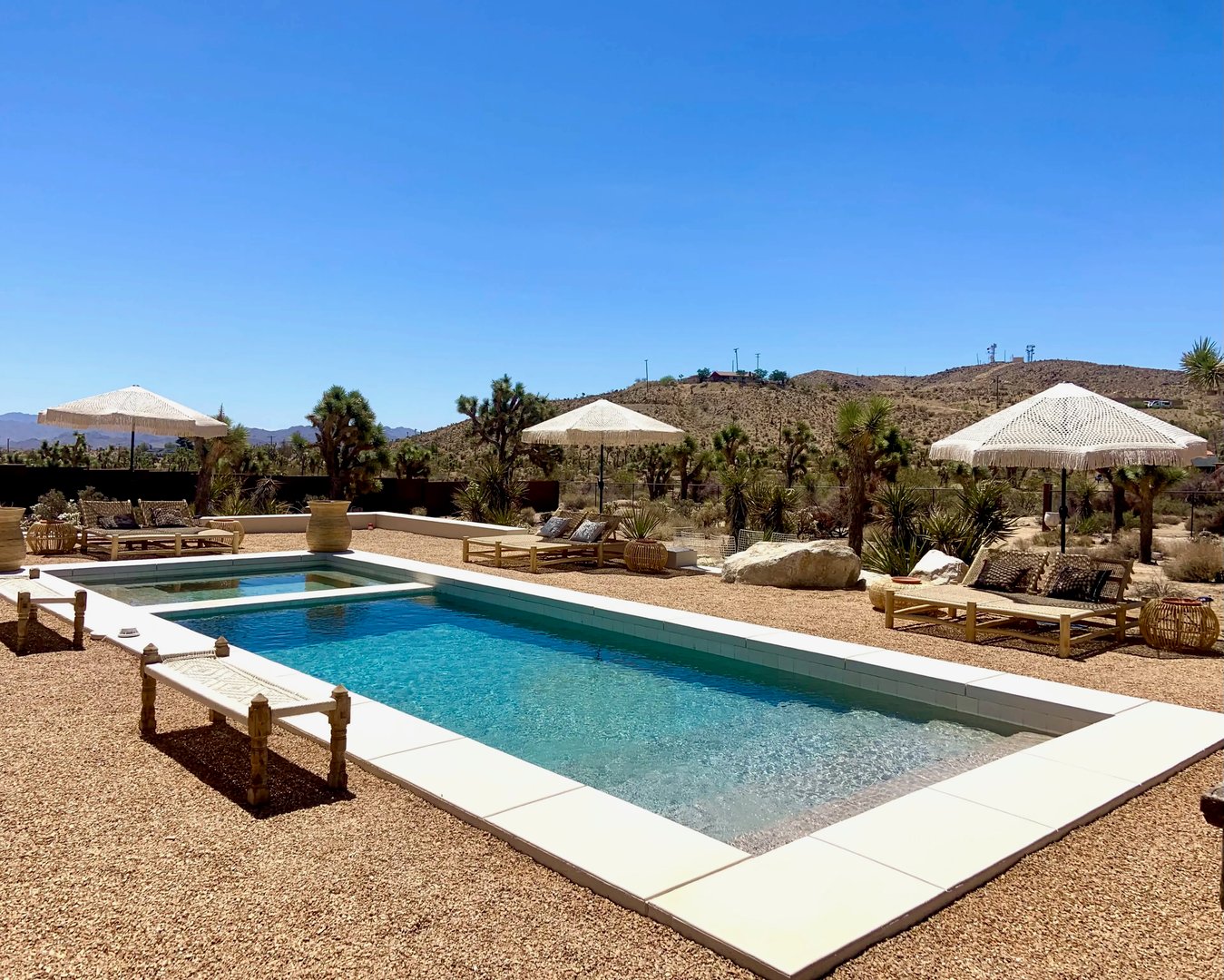 Clear desert rental pool with fringed umbrellas, lounge beds and Joshua trees