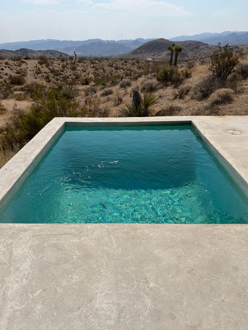 Small square concrete plunge pool with clear teal water overlooking desert mountains