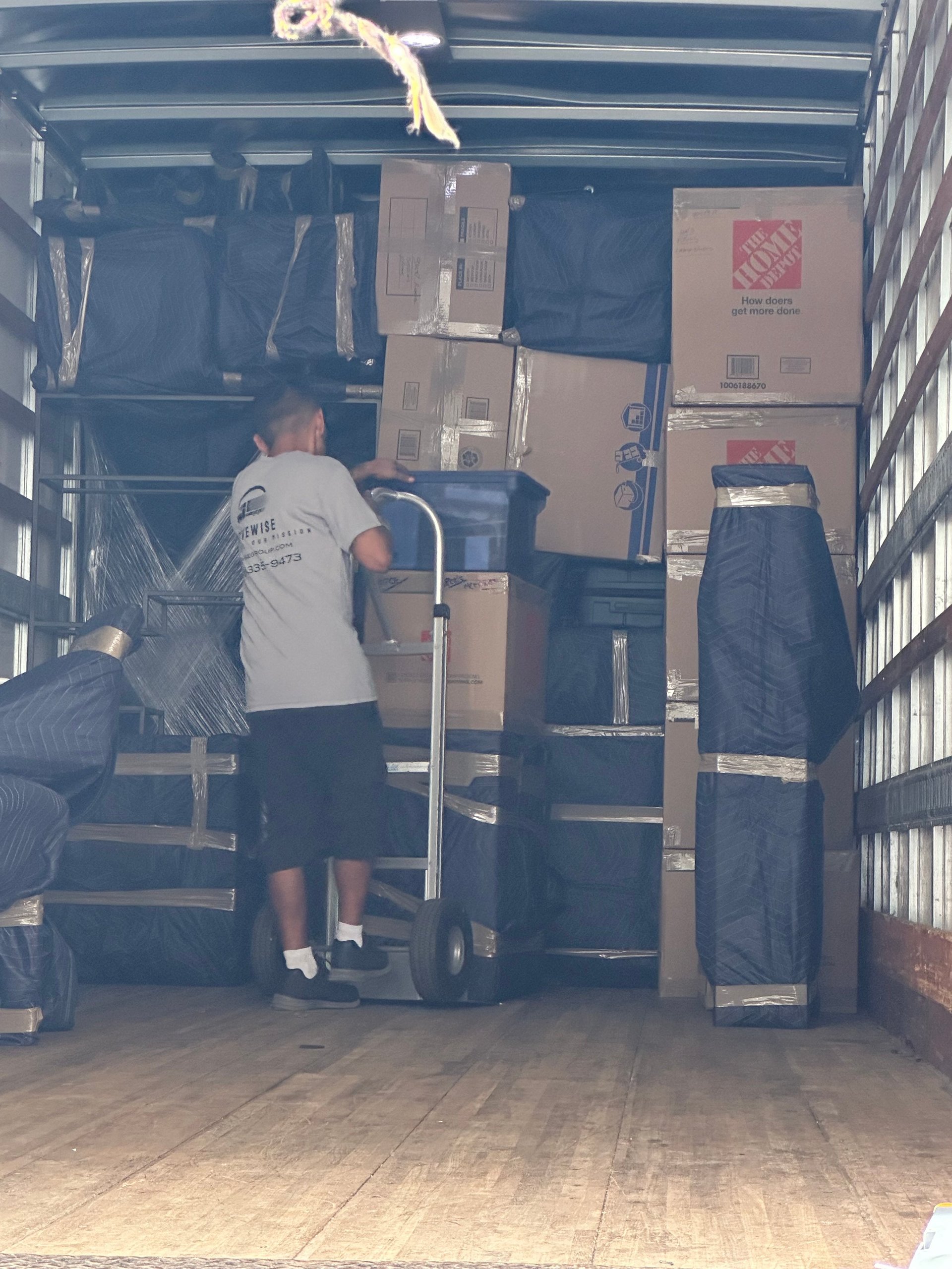 Mover using a hand truck to load boxes into a truck packed with blanket-wrapped furniture