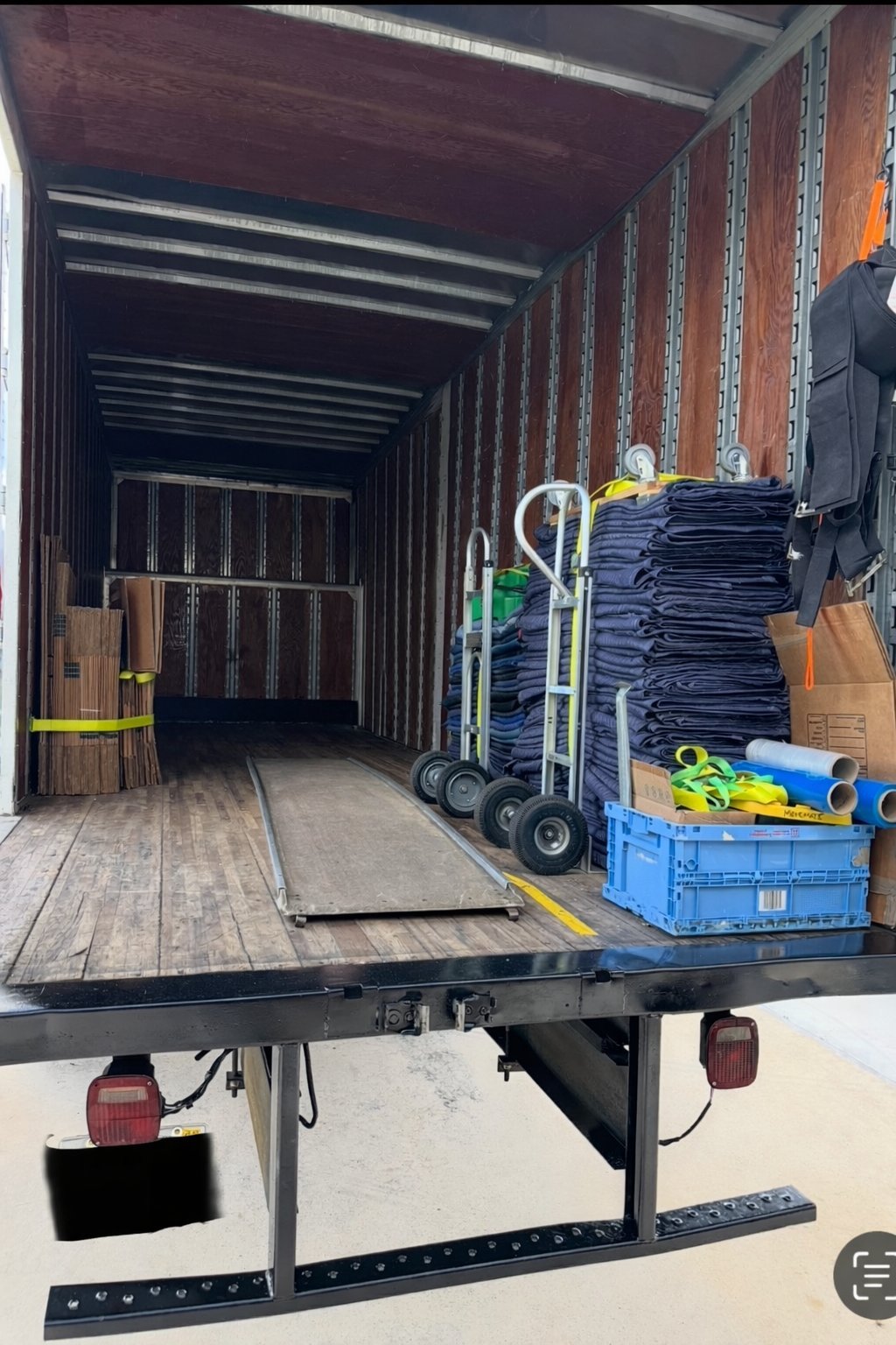 Open Move Mate truck with stacked moving blankets, hand trucks, a loading ramp, straps and flattened boxes