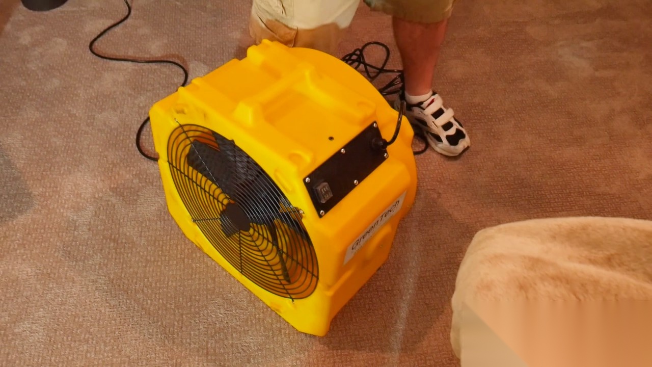 Yellow GreenTech air mover fan on carpet with a person's legs and sneakers nearby
