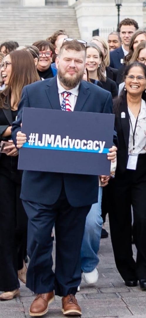 Rusty Havens, founder and CEO of SWLA Abolitionists, holding an #IJMAdvocacy sign while walking with fellow advocates outside a government building