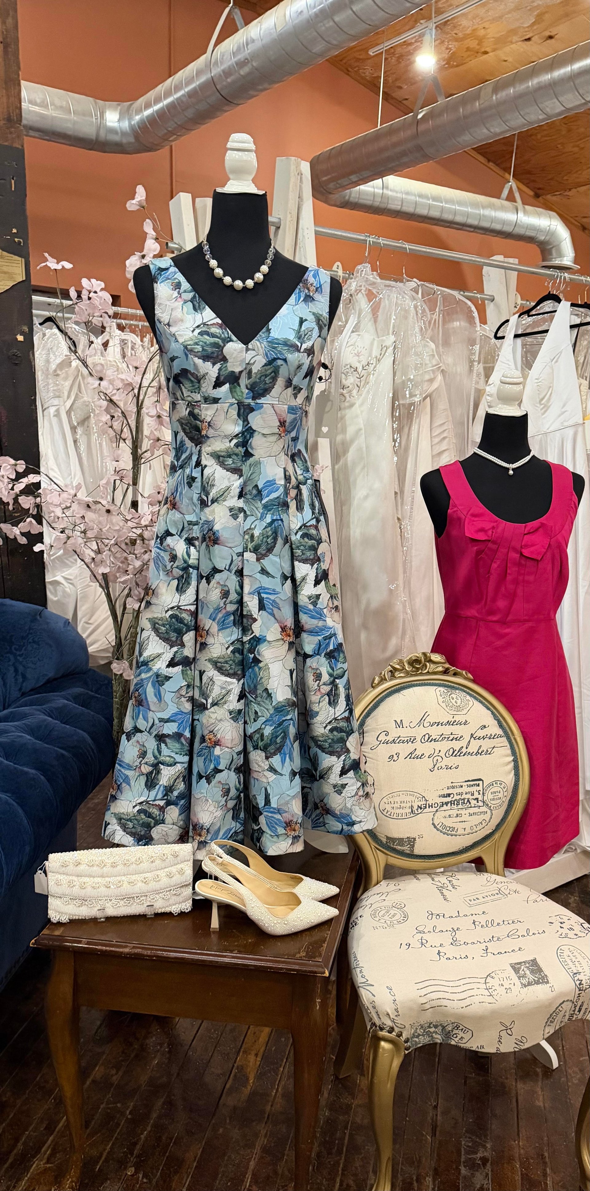 Blue floral dress and a hot-pink dress on dress forms in the boutique