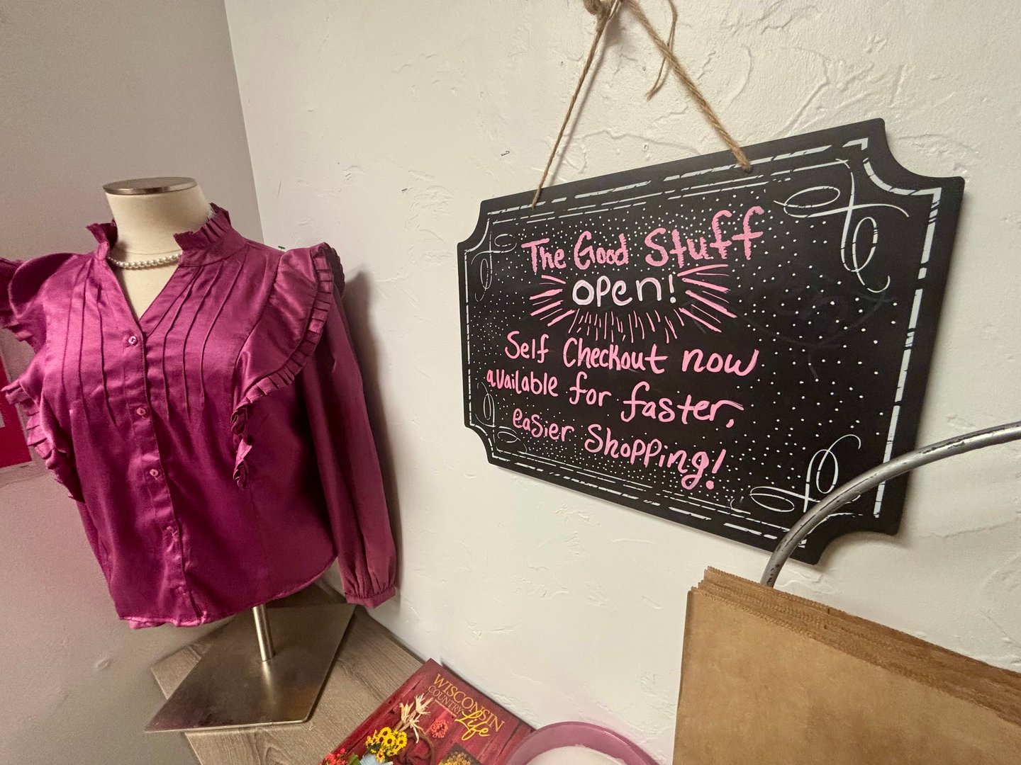 Magenta ruffled blouse on a dress form beside a chalkboard sign announcing The Good Stuff is open