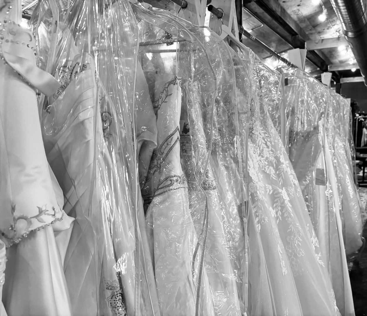 Black and white close-up of a rack of wedding gowns in clear garment bags