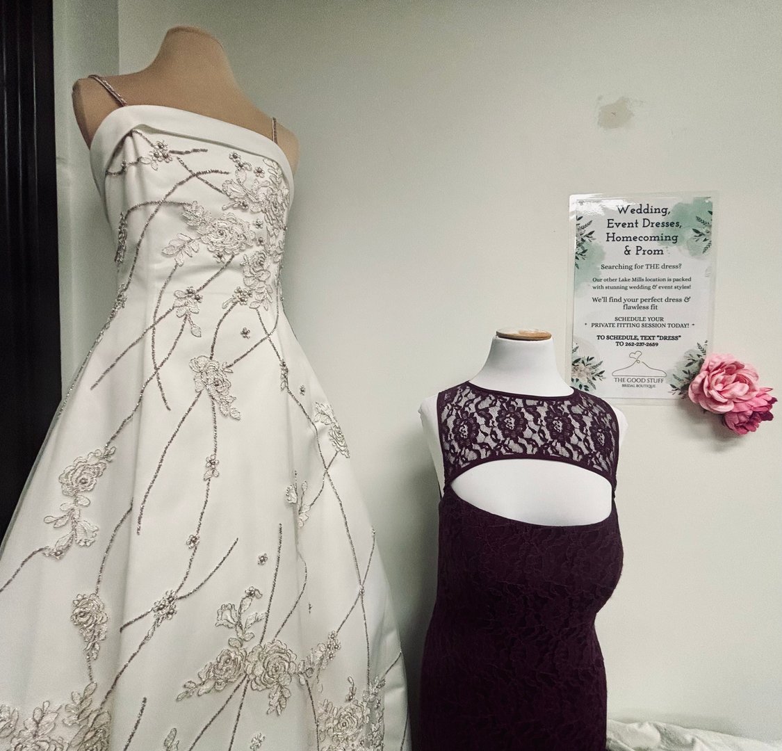 Beaded white wedding gown and plum lace bridesmaid dress beside The Good Stuff private fitting sign