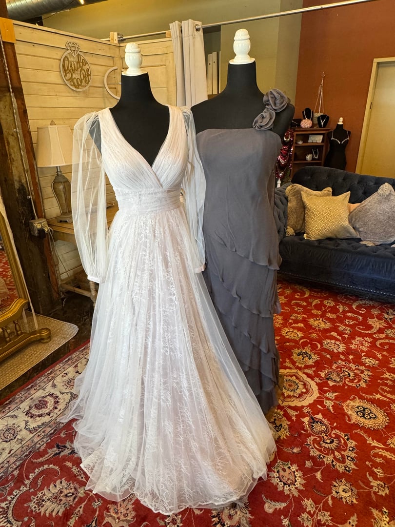 Long-sleeve white lace wedding gown and grey tiered dress on mannequins