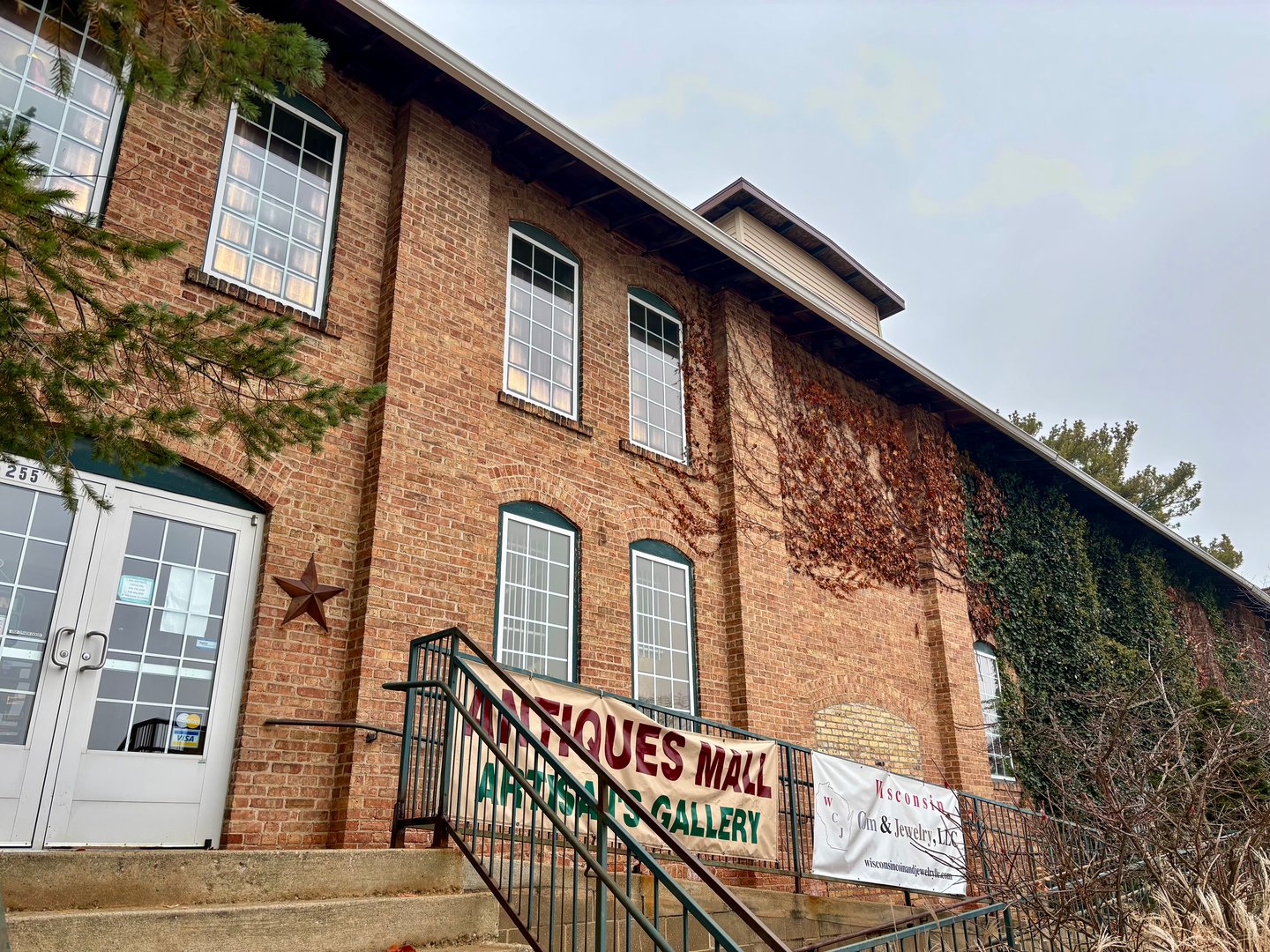 Brick building exterior with ivy, double doors, and an Antiques Mall Artisans Gallery banner on the railing